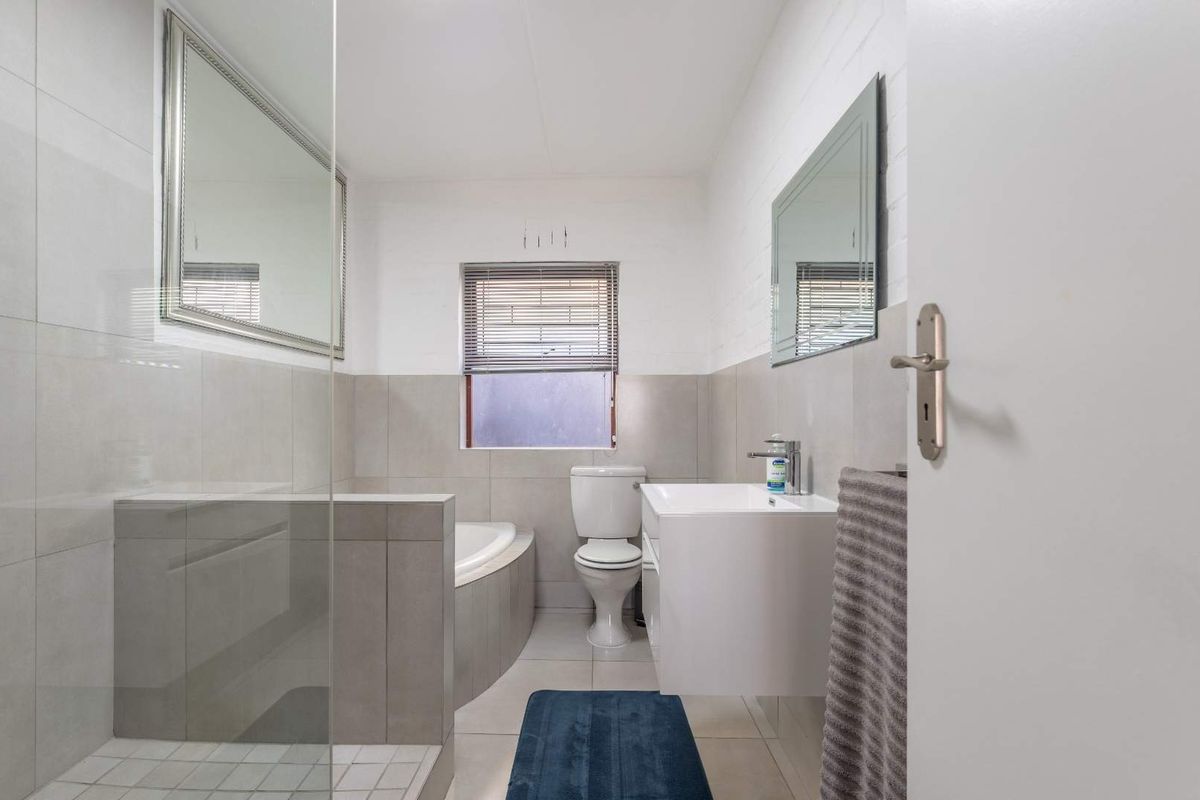 A modern, well-maintained bathroom featuring a glass-enclosed shower, a built-in bathtub, a wall-mounted vanity, and neutral tiled finishes.