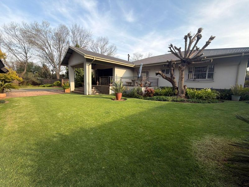 A well-maintained rear exterior view featuring a spacious lawn, landscaped garden, and a covered patio area with metal roofing.