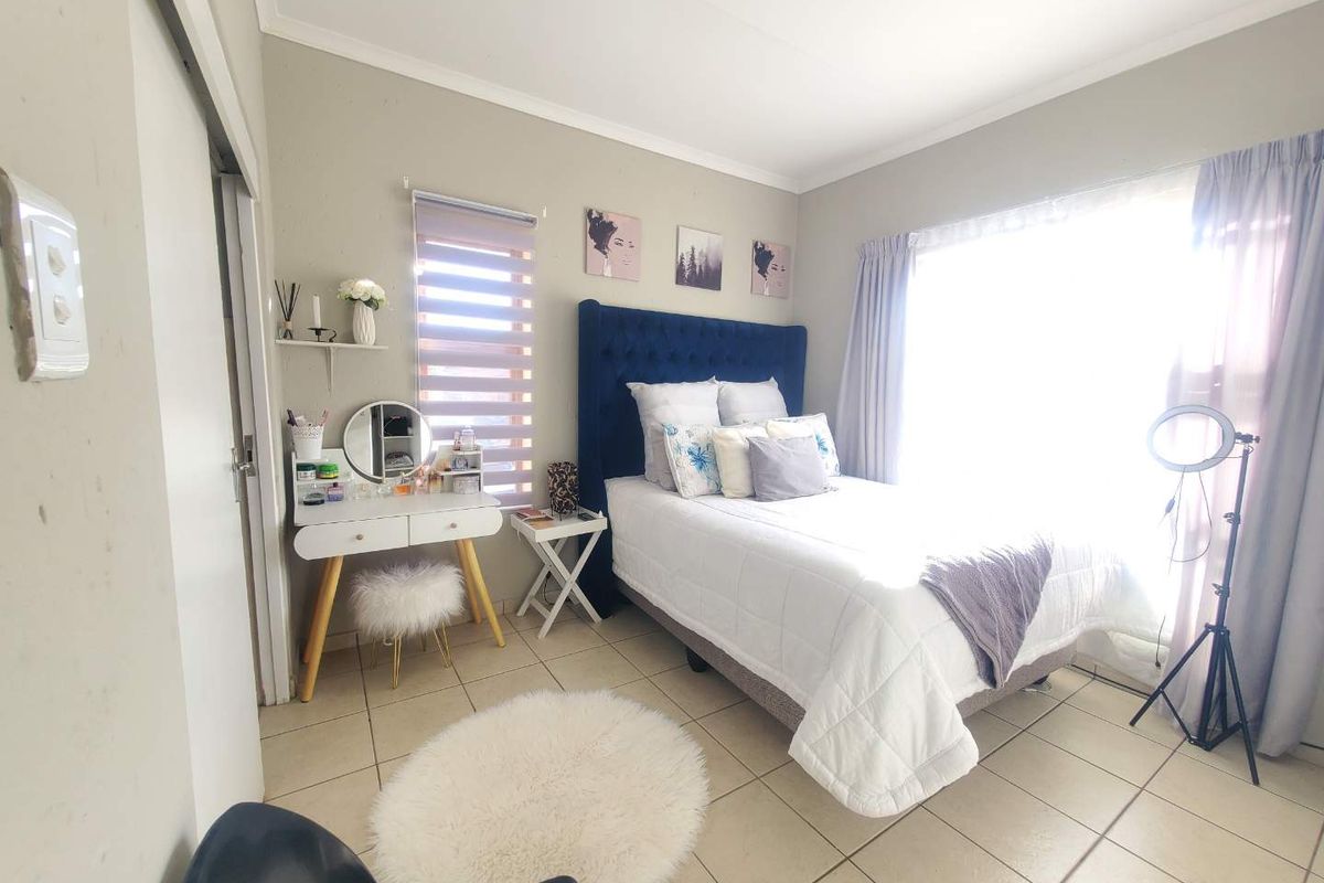 A well-lit bedroom featuring neutral wall tones, tiled flooring, and a large window with fitted curtains.