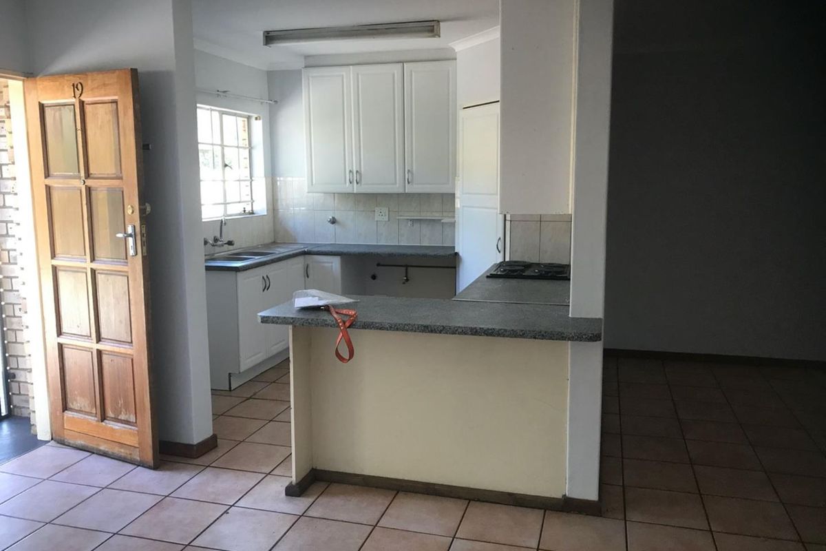 A functional kitchen featuring white cabinetry, laminate countertops, a built-in hob, and tiled flooring, offering a blank canvas for potential modernization.