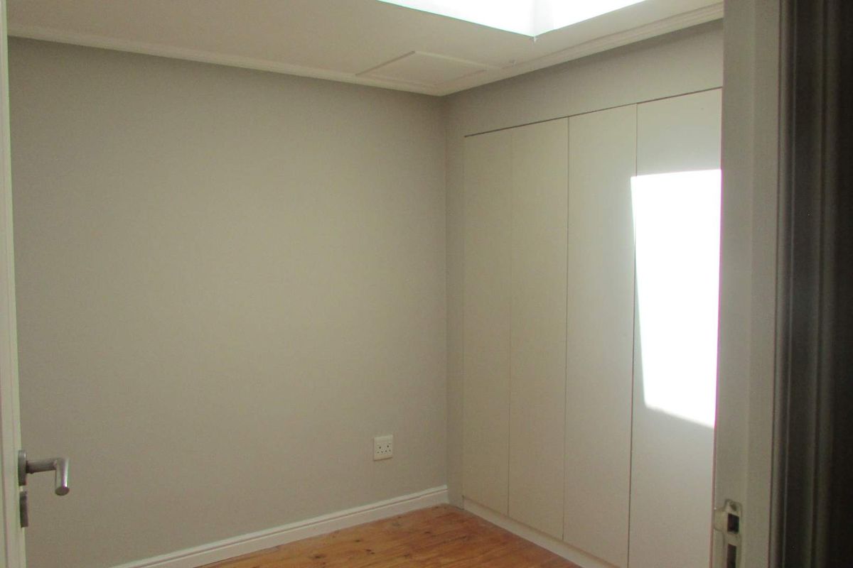 A clean, empty bedroom featuring neutral walls, timber flooring, and built-in floor-to-ceiling cabinetry.
