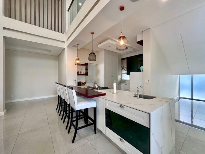 Modern open-plan kitchen featuring a large stone-topped island with integrated sink, stylish pendant lighting, and a double-volume ceiling creating a spacious, airy atmosphere.