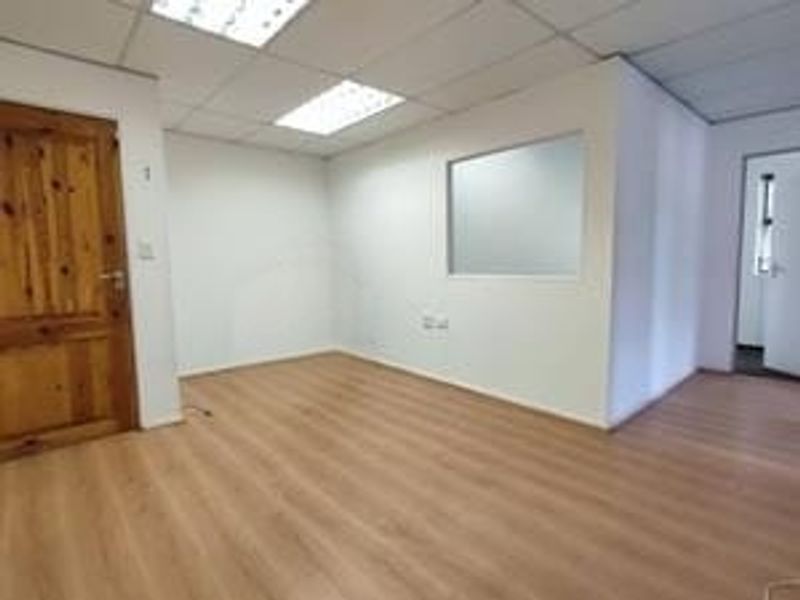 A vacant office space featuring laminate flooring, a suspended ceiling with recessed lighting, and an internal glass partition.