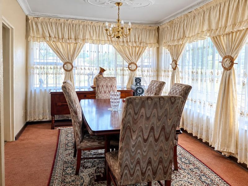 A traditional dining room featuring decorative ceiling cornices, a central ceiling rose, and a classic chandelier, offering a formal space for family meals.