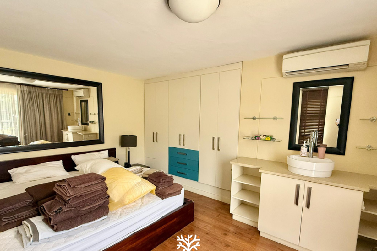 Bedroom featuring built-in wardrobes, an integrated vanity with basin, wood-look flooring, and a wall-mounted air conditioning unit.