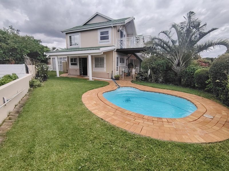 Rear view of a two-story townhouse featuring a swimming pool, covered patio, and an upper-level balcony set within a private garden.