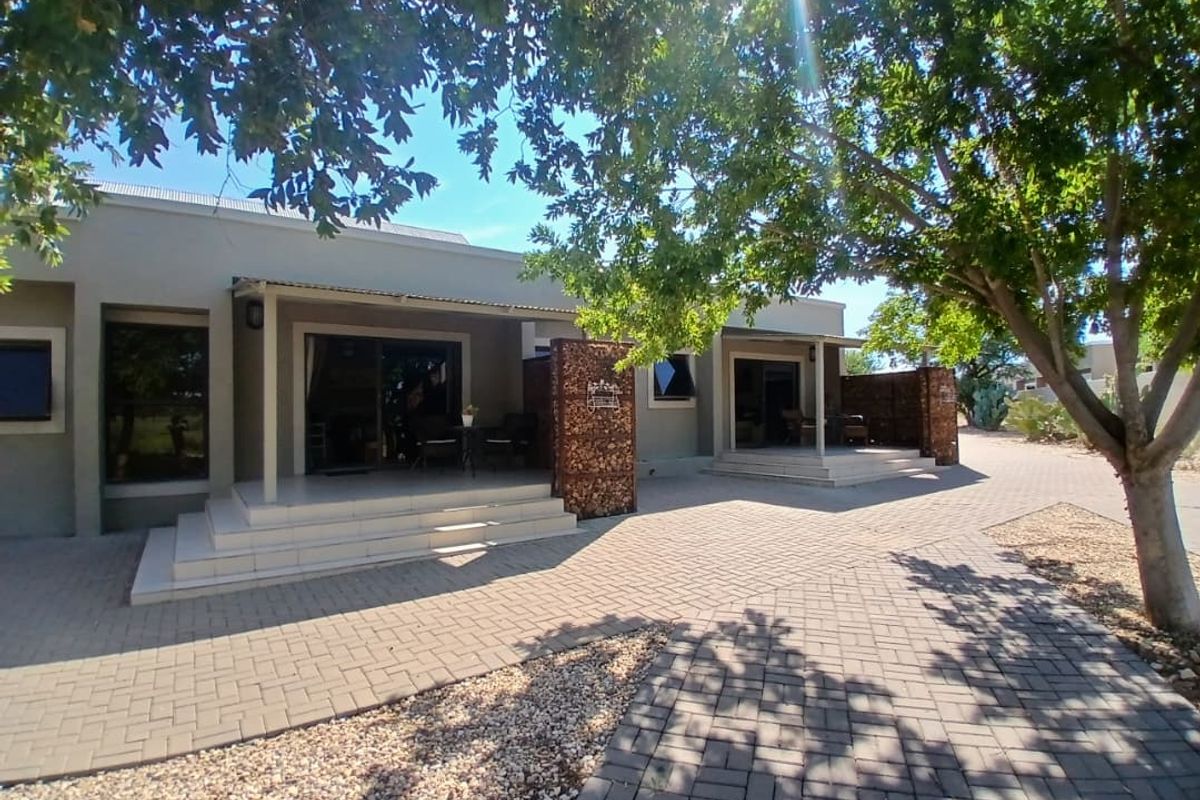 A view of the exterior rear facade featuring paved patio areas, covered walkways, and stone-clad feature pillars set within a landscaped garden.