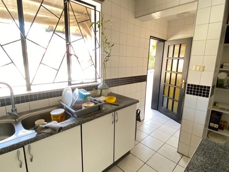 Functional kitchen featuring granite countertops, double bowl sink, tiled splashback, and recessed lighting, with direct access to an exterior doorway.