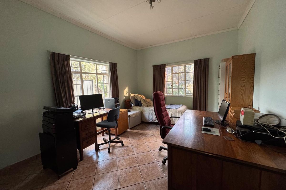 A multi-purpose bedroom featuring tiled flooring, dual windows providing natural light, and ample space for a home office setup.