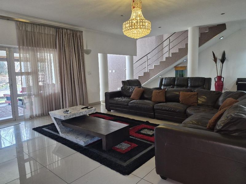 Spacious living area featuring polished porcelain floor tiles, a feature staircase with metal balustrade, and direct access to the patio through sliding glass doors.