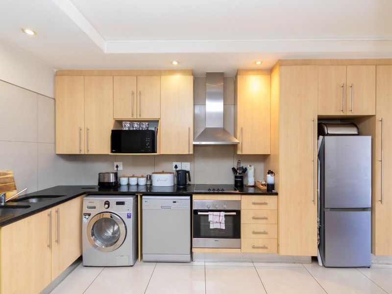 A modern kitchen featuring light-wood cabinetry, black granite countertops, stainless steel appliances, and recessed lighting in a clean, functional layout.