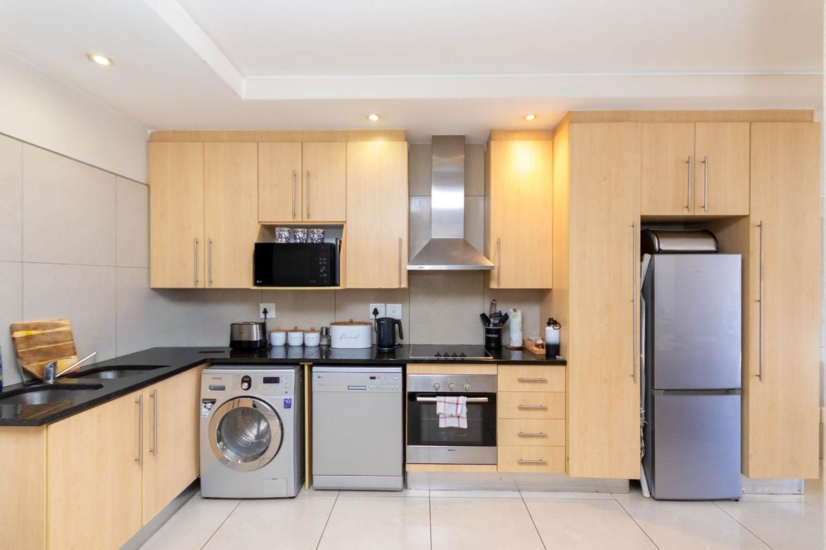 A modern kitchen featuring light-wood cabinetry, black granite countertops, stainless steel appliances, and recessed lighting in a clean, functional layout.