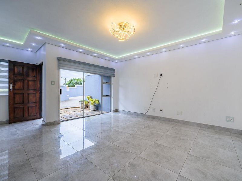 A bright, empty living area featuring modern recessed cove lighting, large format floor tiles, and direct access to an outdoor patio through sliding glass doors.