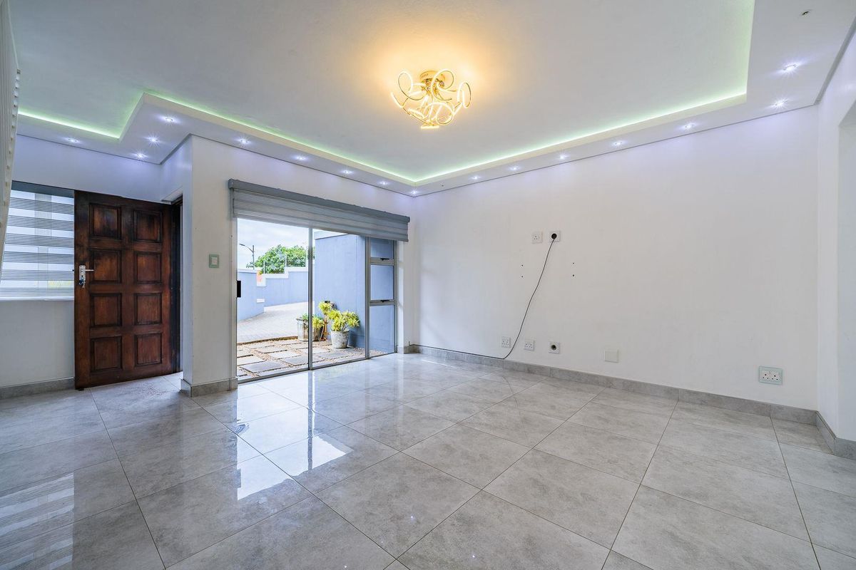A bright, empty living area featuring modern recessed cove lighting, large format floor tiles, and direct access to an outdoor patio through sliding glass doors.
