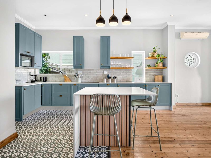 Modern kitchen featuring blue cabinetry, stone countertops, a central island with timber detailing, subway tile backsplash, and a mix of timber and patterned tile flooring.