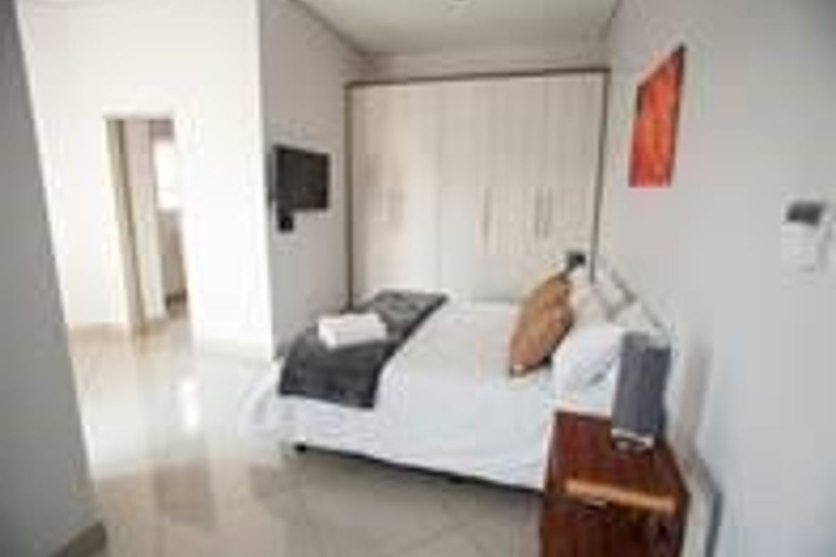 A well-maintained bedroom featuring neutral tiled flooring, built-in cupboards, and recessed downlighting, offering a clean and functional living space.