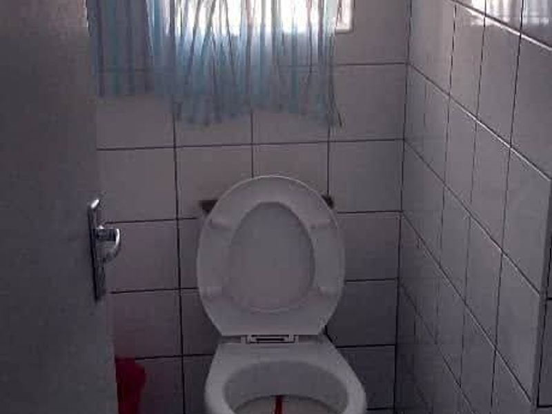 A compact, tiled bathroom featuring a standard toilet and a window with security bars.