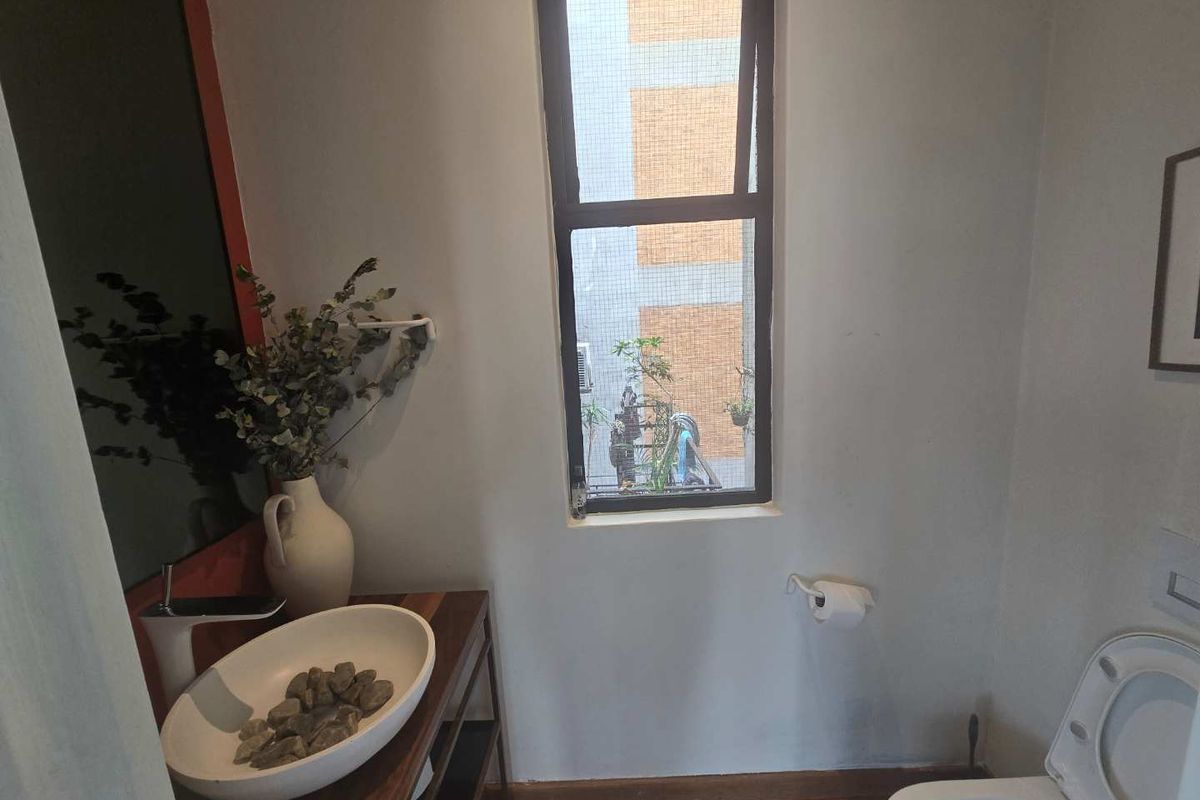 A compact bathroom featuring a modern vessel sink on a wooden vanity, a wall-mounted toilet, and a window providing natural light.