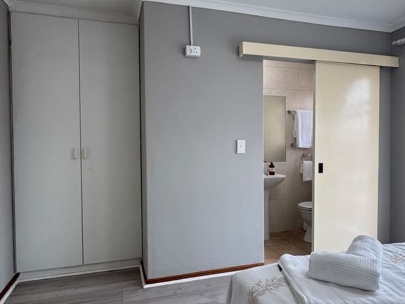 Bedroom featuring laminate flooring, built-in cupboards, and a sliding door providing access to an en-suite bathroom.
