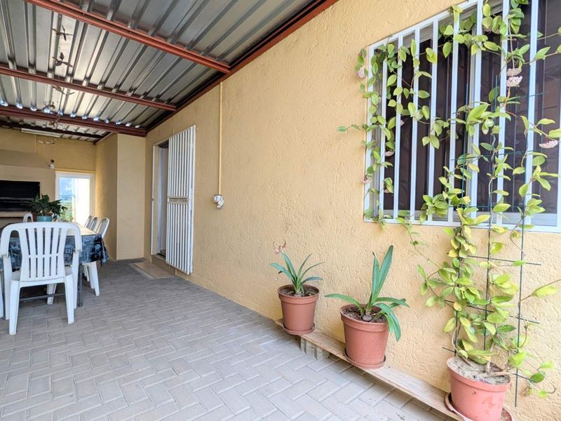 Covered outdoor patio area featuring paved flooring, a built-in braai, and security bars on the windows, providing a functional space for outdoor dining.