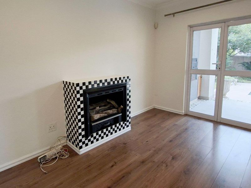 A bright living room featuring laminate flooring, a distinctive checkered fireplace, and glass doors providing access to the outdoor patio area.