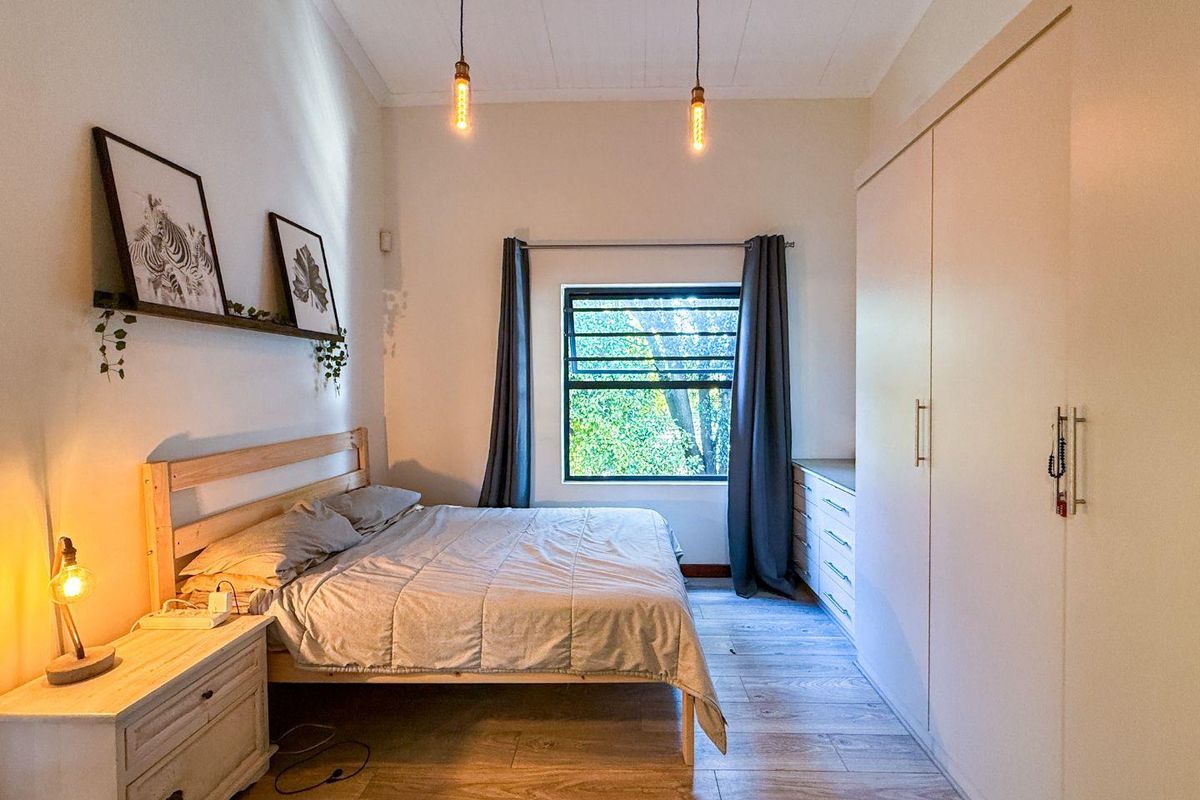A well-lit bedroom featuring built-in floor-to-ceiling wardrobes, wood-look tiled flooring, and a large window providing natural light.