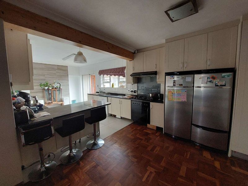Open-plan kitchen featuring built-in cabinetry, a breakfast bar, gas hob, and oven, seamlessly flowing into the adjacent living area with parquet flooring.