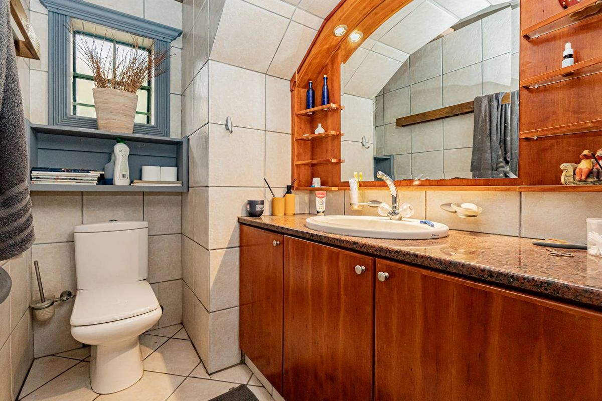 A functional bathroom featuring a built-in wooden vanity with granite countertop, integrated sink, wall-mounted mirror, and tiled finishes throughout.