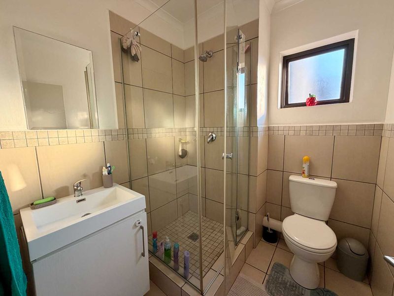 A functional bathroom featuring a glass-enclosed shower, a modern vanity with basin, and neutral wall tiling.