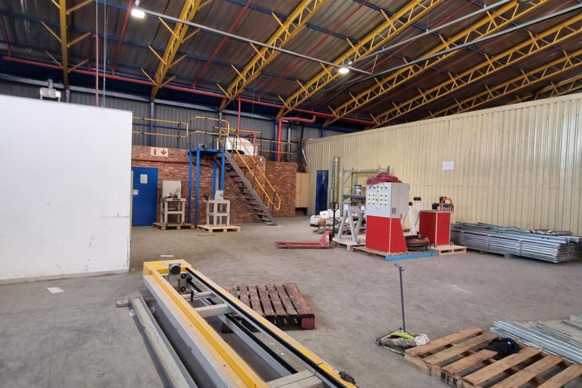Spacious industrial warehouse featuring high-clearance steel truss roofing, concrete flooring, and integrated mezzanine access with metal staircase.