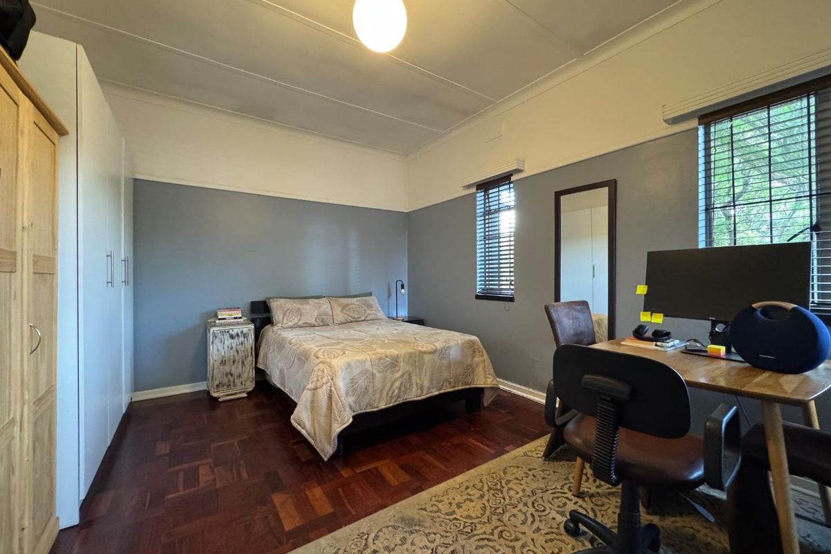 A well-maintained bedroom featuring polished parquet flooring, built-in wardrobes, and dual-tone wall finishes with natural light from two windows.