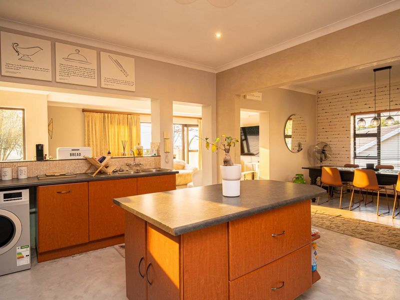 Open-plan kitchen and dining area featuring a central island, laminate cabinetry, and an exposed brick feature wall in the dining space.