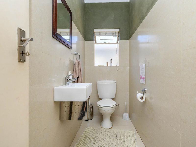 A compact guest bathroom featuring a wall-mounted basin, toilet, and neutral wall tiling with a contrasting painted upper section.