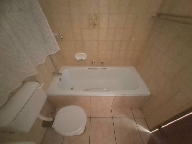 A dated bathroom featuring a standard bathtub, toilet, and neutral wall and floor tiling, offering potential for a modern renovation.