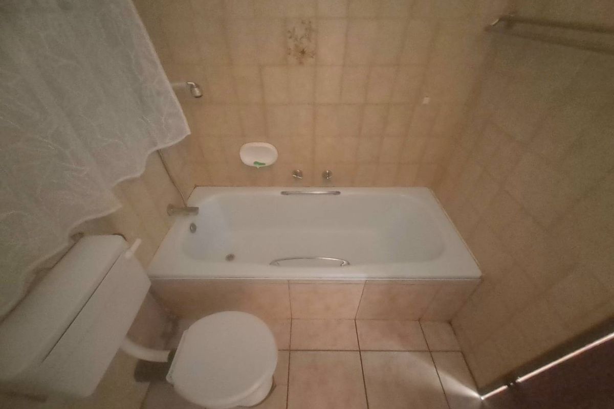 A dated bathroom featuring a standard bathtub, toilet, and neutral wall and floor tiling, offering potential for a modern renovation.