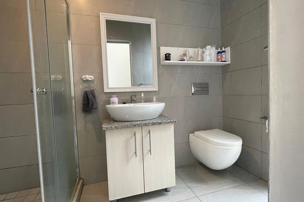 Modern bathroom featuring a wall-mounted toilet, glass shower enclosure, and a vanity unit with a vessel sink and granite countertop.