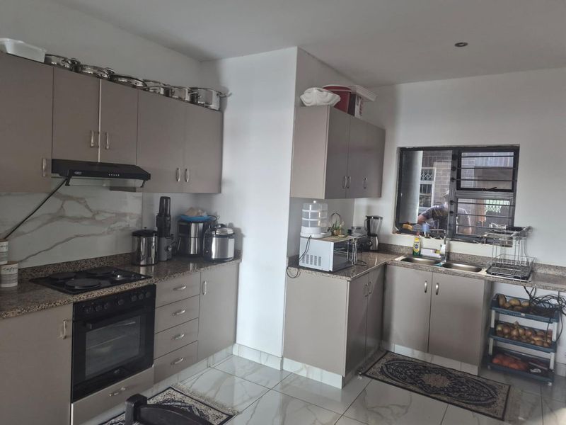 A functional kitchen featuring modern taupe cabinetry, granite countertops, built-in oven, electric hob, and a double sink with tiled flooring.
