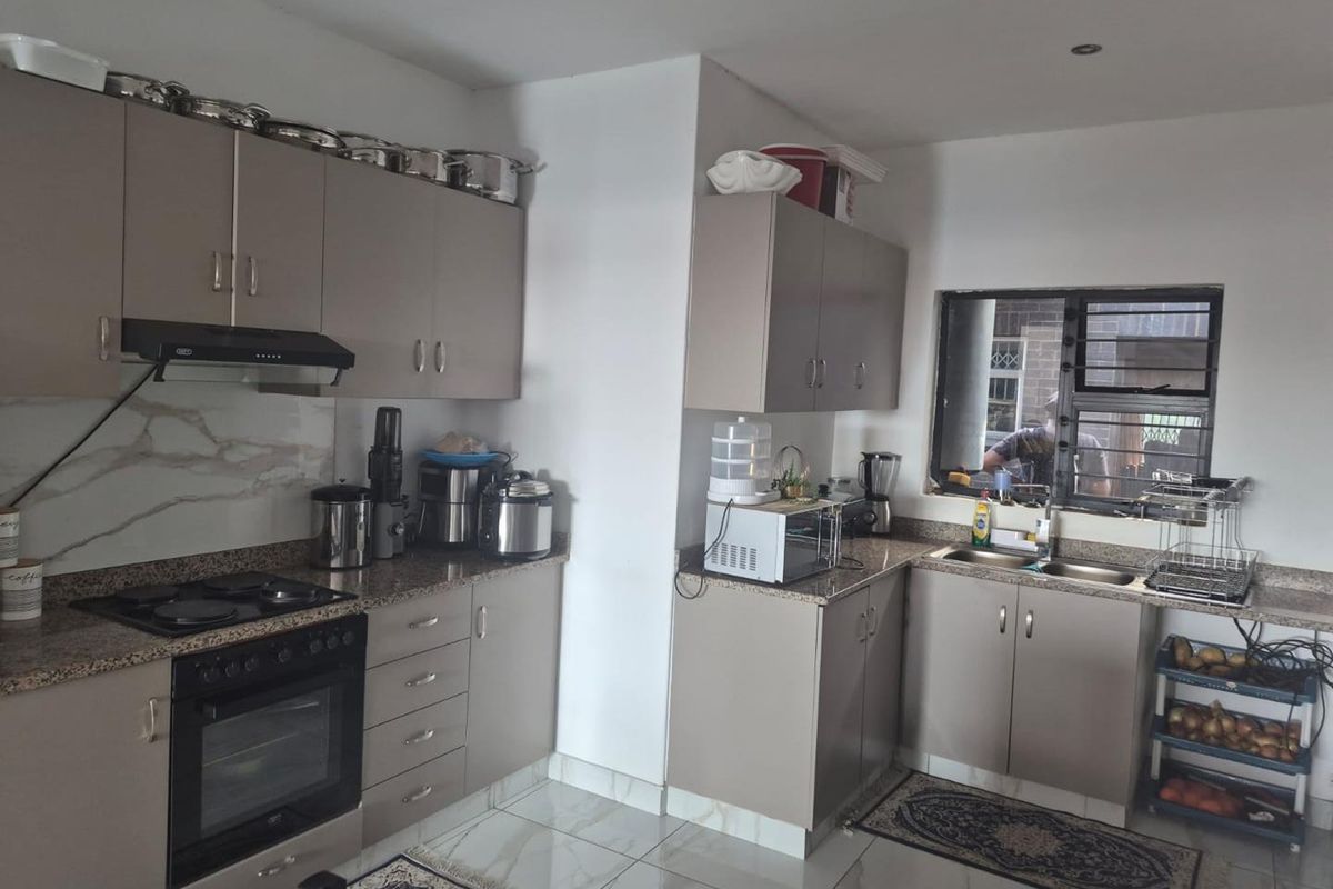 A functional kitchen featuring modern taupe cabinetry, granite countertops, built-in oven, electric hob, and a double sink with tiled flooring.