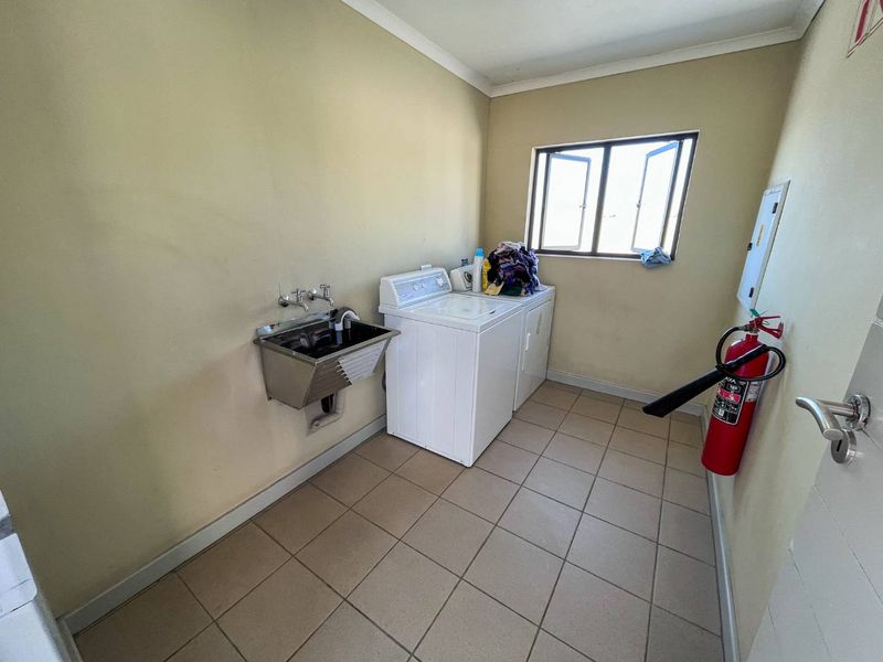 A functional laundry room featuring tiled flooring, a wall-mounted stainless steel utility sink, and dedicated space for laundry appliances.