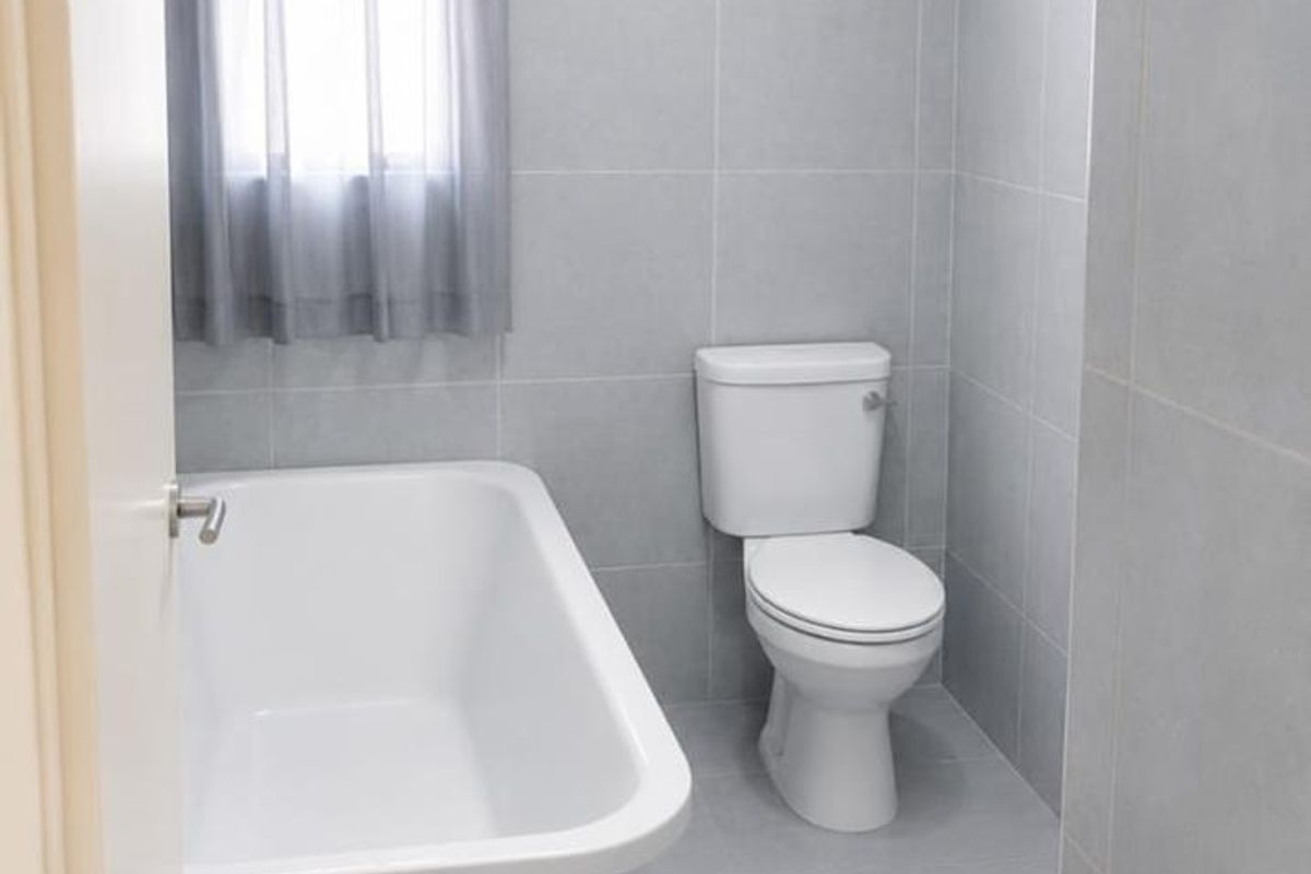 A clean, modern bathroom featuring a freestanding bathtub, a white toilet, and neutral grey floor-to-ceiling wall tiles.