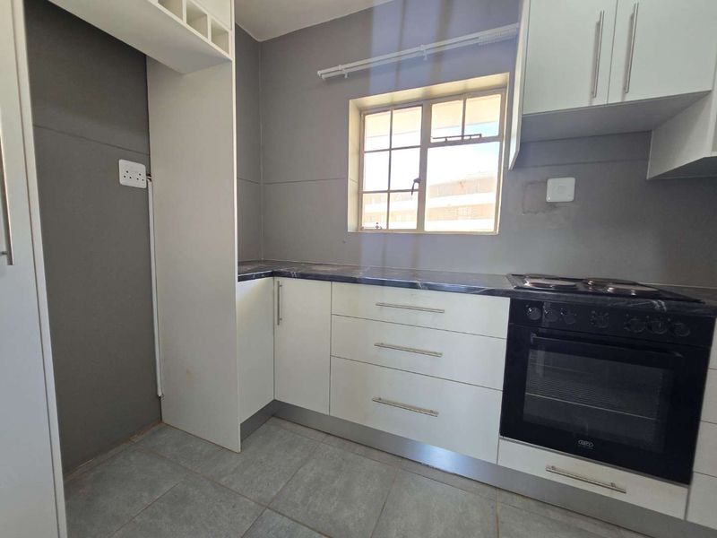 A clean and functional kitchen featuring white cabinetry, dark laminate countertops, a built-in oven, and an electric hob with tiled flooring.