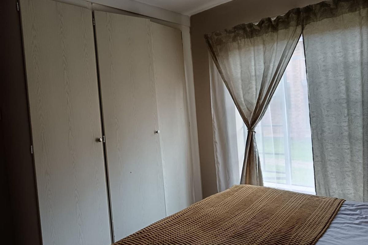 A bedroom featuring built-in wooden wardrobes and a window with natural light.