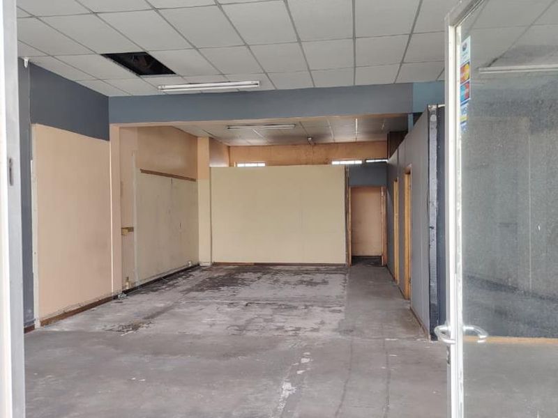 An empty, open-plan commercial space featuring a suspended ceiling, fluorescent lighting, and worn concrete flooring, ready for renovation or fit-out.