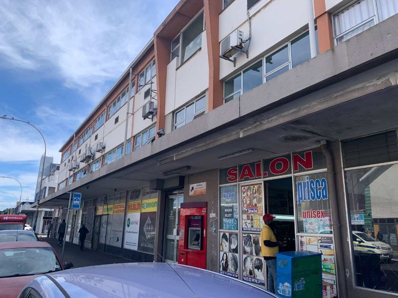 Street-level view of a multi-story commercial office building featuring ground-floor retail storefronts, a covered pedestrian walkway, and exterior-mounted air conditioning units.