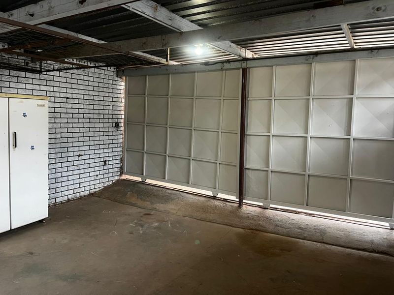 A functional garage space featuring exposed brick walls, concrete flooring, and large sliding metal garage doors.