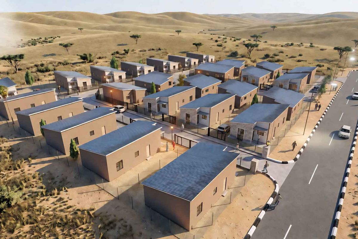An aerial view of a modern townhouse development featuring multiple residential units, paved access roads, and perimeter security fencing in a desert landscape.