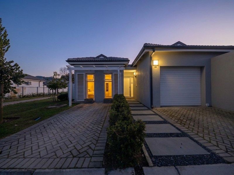 Front elevation of a modern townhouse featuring a paved driveway, single garage, and a welcoming entrance with pergola detail at dusk.