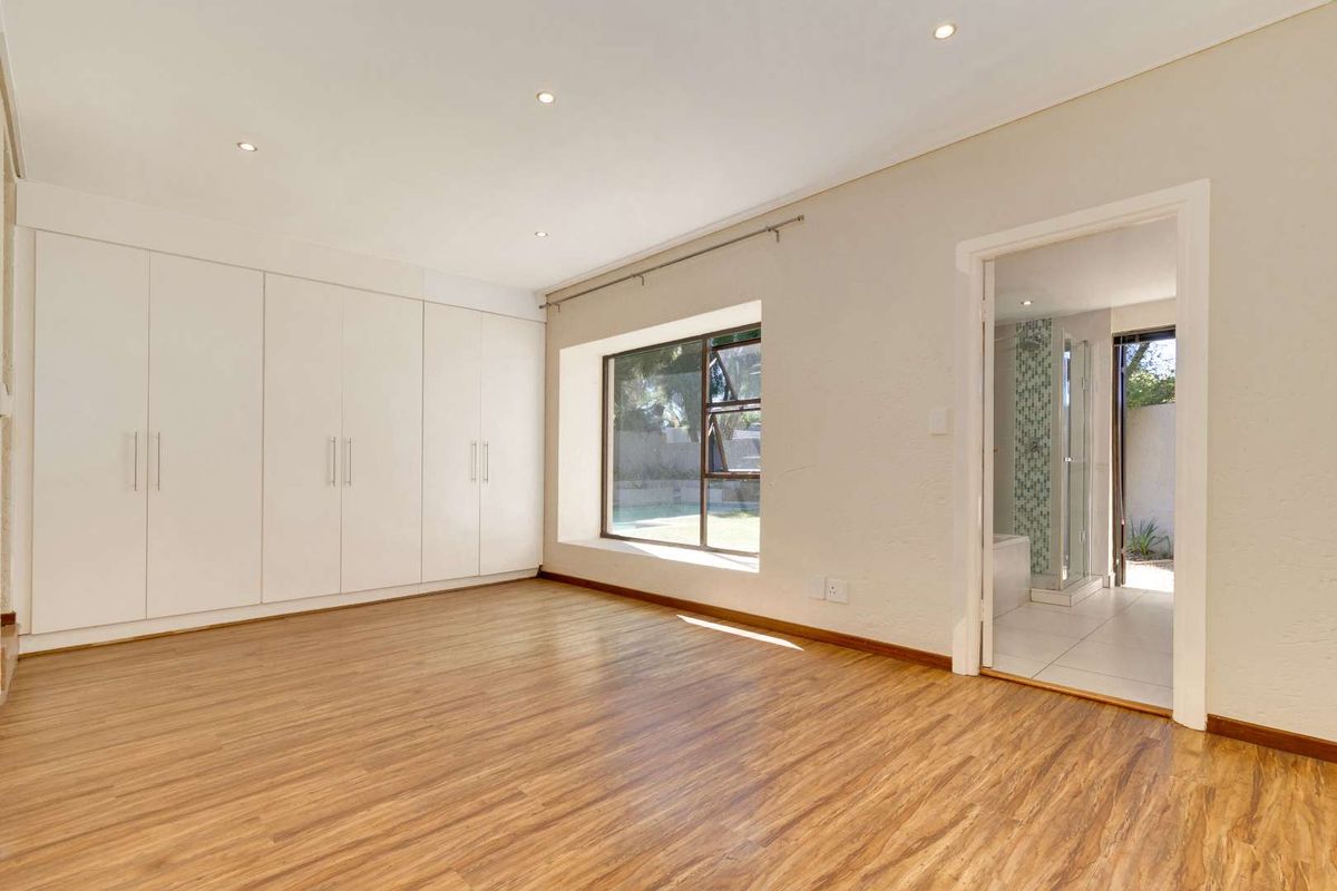 Spacious bedroom featuring built-in cupboards, laminate flooring, and recessed downlights, with an adjoining en-suite bathroom.