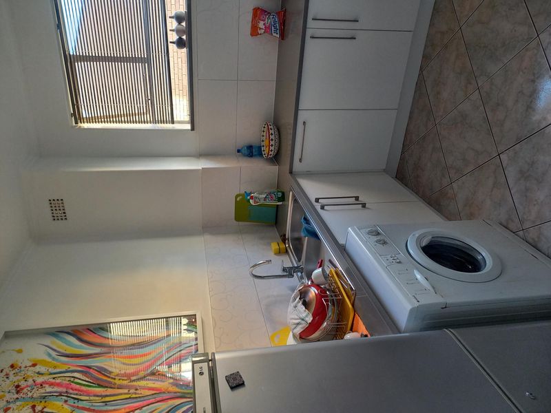 A functional kitchen featuring white cabinetry, tiled splashbacks, laminate countertops, a stainless steel sink, and integrated space for a washing machine.