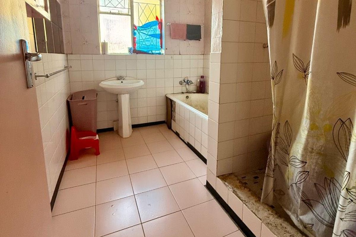 A dated bathroom featuring a pedestal basin, a built-in bathtub, and a shower area, requiring significant renovation and modernization of finishes.
